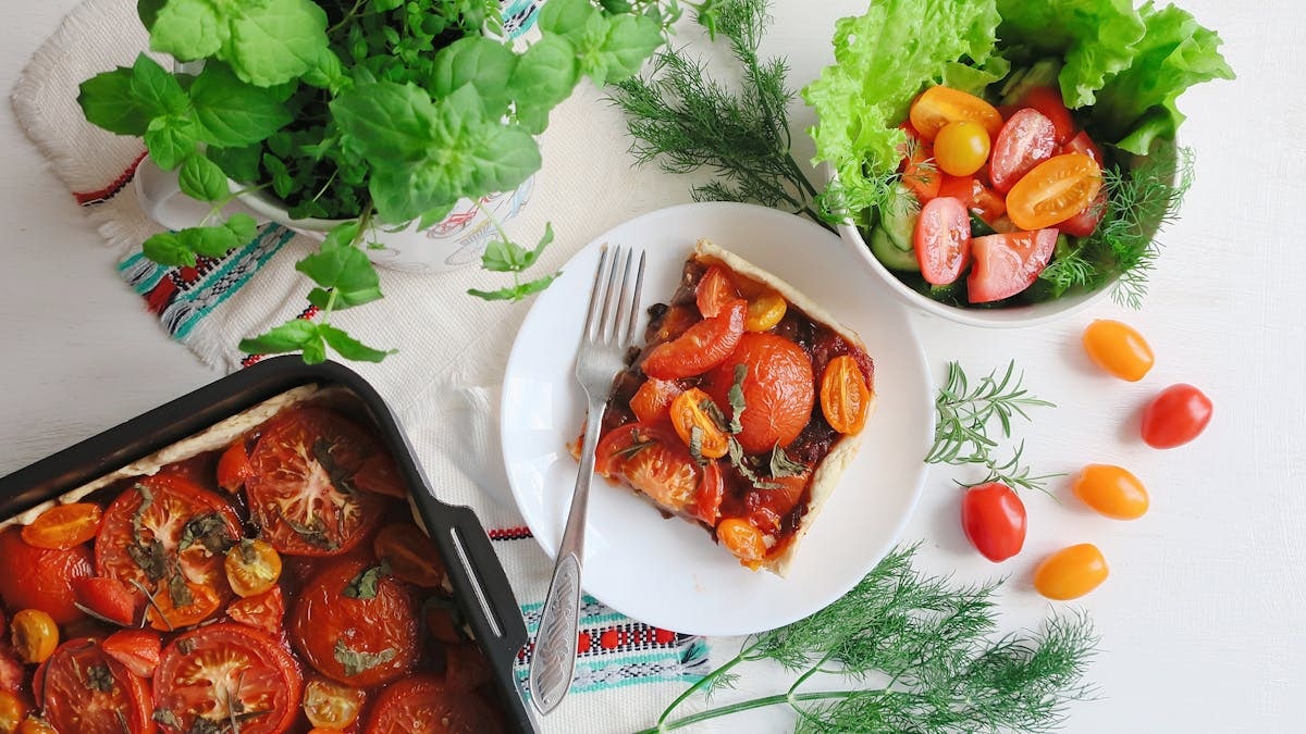 Top view of a vibrant tomato tart paired perfectly with a fresh salad and herbs.